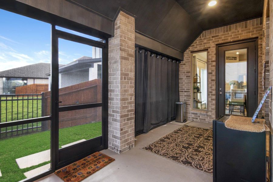 This photo showcases a cozy screened-in porch for those year round beautiful nights also featuring brick walls post and outdoor curtains for privacy. The space offers a view of the fenced backyard, ideal for relaxing or entertaining.