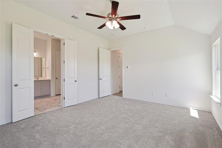 Unfurnished bedroom with ceiling fan, connected bathroom, light carpet, and vaulted ceiling