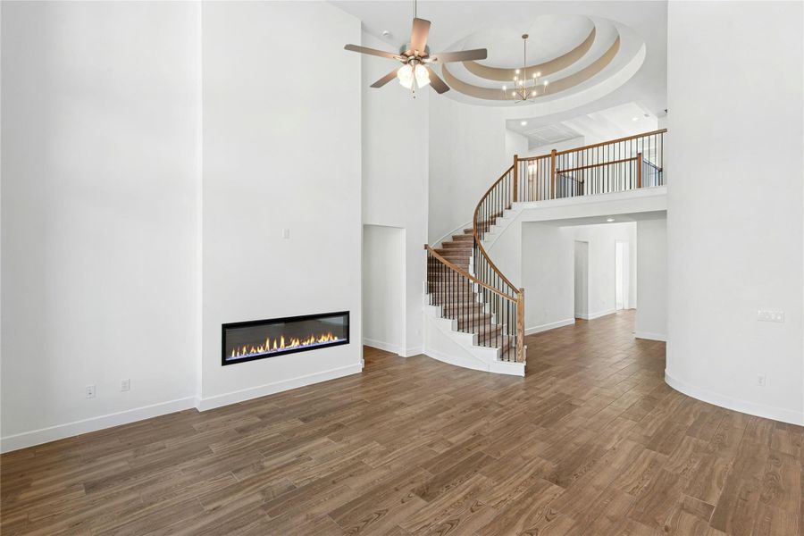 Unfurnished living room with a glass covered fireplace, stairway, wood finished floors, a ceiling fan, and a tray ceiling