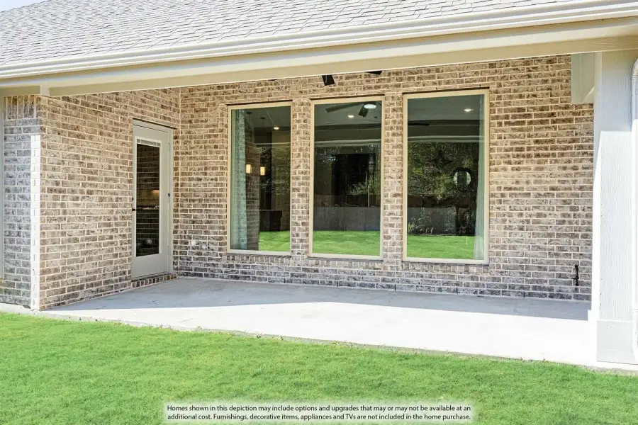Brick home exterior with large windows, back door, and concrete patio overlooking green lawn