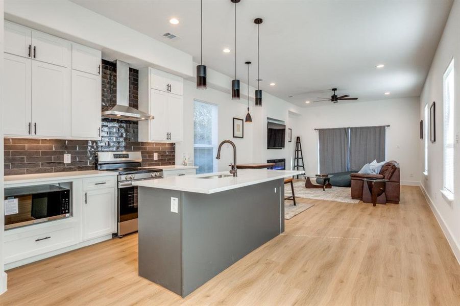 Kitchen with white cabinets, appliances with stainless steel finishes, and wall chimney range hood