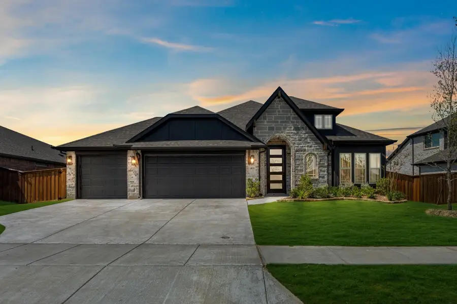 Single-story home with stone exterior, three-car garage, dark trim, and green front lawn at dusk Single-story home with stone exterior, three-car garage, dark trim, and green front lawn at dusk