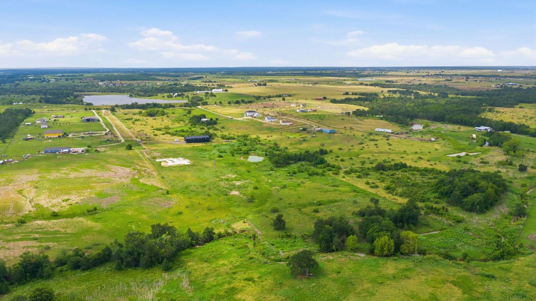 Expansive green acreage with distant homes and a tranquil pond, offering serene rural living.