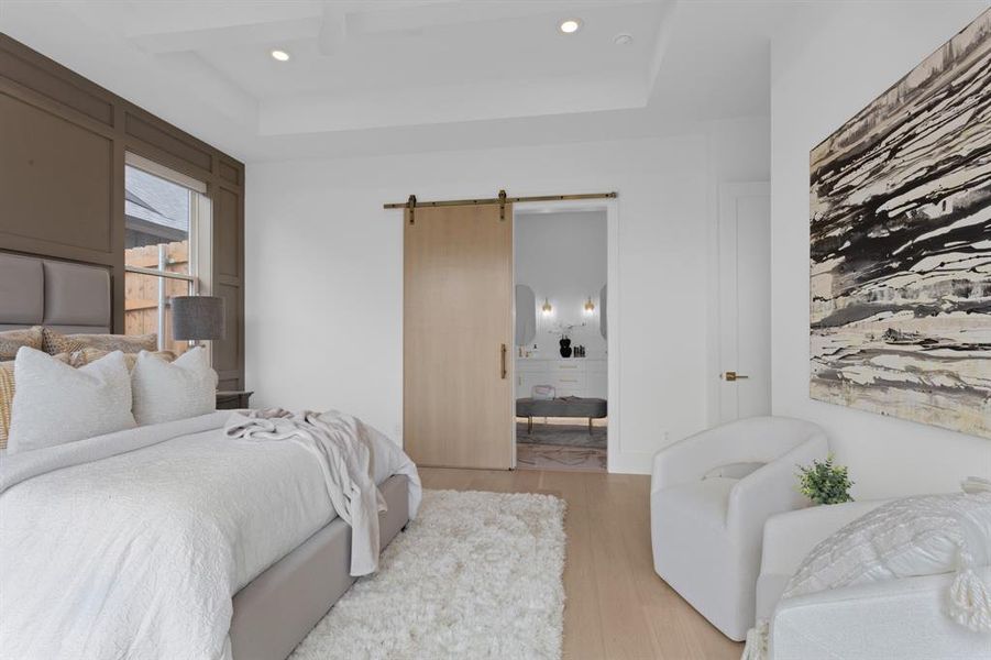 Bedroom featuring a barn door, light wood-type flooring, recessed lighting, and a raised ceiling Bedroom featuring a barn door, light wood-type flooring, recessed lighting, and a raised ceiling