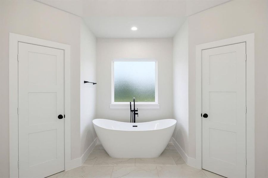 Freestanding white soaking tub with matte black floor-mounted faucet and frosted window