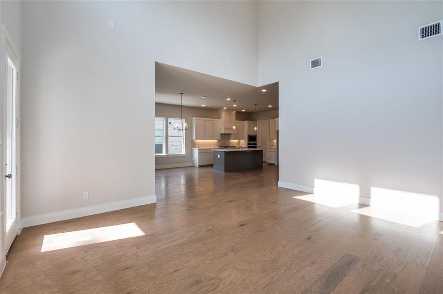 Unfurnished living room featuring a towering ceiling, an inviting chandelier, sink, and hardwood / wood-style floors