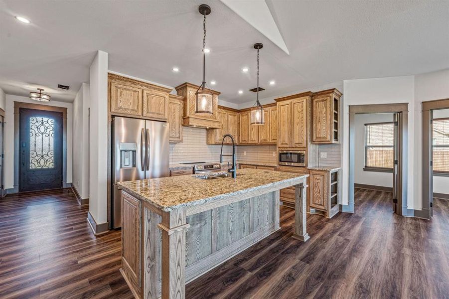 Kitchen featuring decorative backsplash, a kitchen island with sink, appliances with stainless steel finishes, light stone counters, and recessed lighting