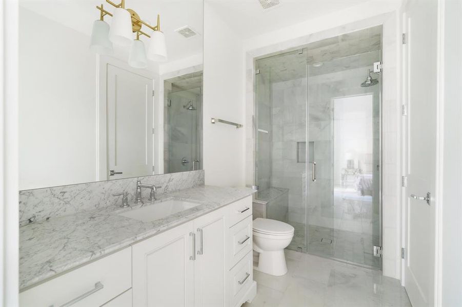 The en suite ground floor bathroom features a stone countertop with furniture-style cabinetry and a frameless glass walk-in shower with bench seating. (photo of interior model home with smaller floor plan)