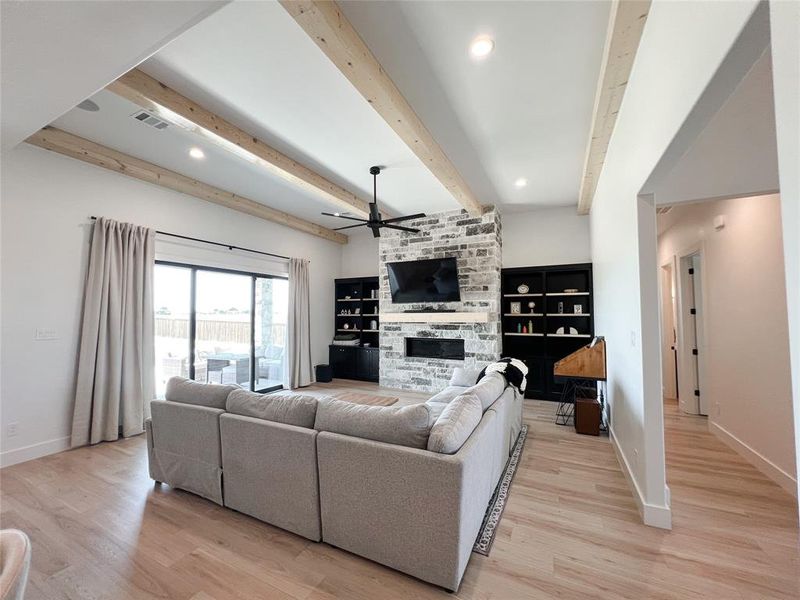 Living room with beamed ceiling, ceiling fan, a stone fireplace, recessed lighting, and light wood finished floors