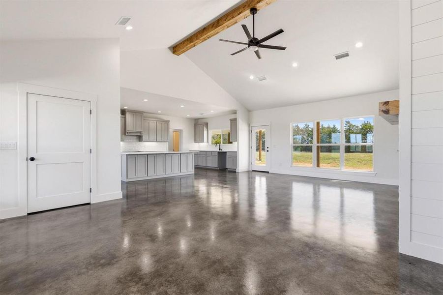 Spacious living area featuring polished concrete floors, an exposed wood beam, a ceiling fan, and large windows offering exterior views