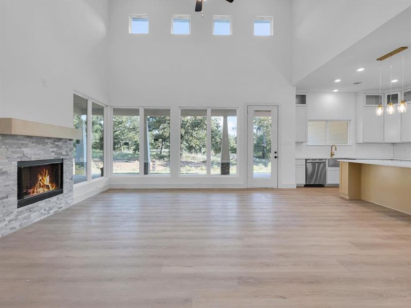 Unfurnished living room with healthy amount of natural light, light wood-style floors, a high ceiling, a stone fireplace, and recessed lighting Unfurnished living room with healthy amount of natural light, light wood-style floors, a high ceiling, a stone fireplace, and recessed lighting