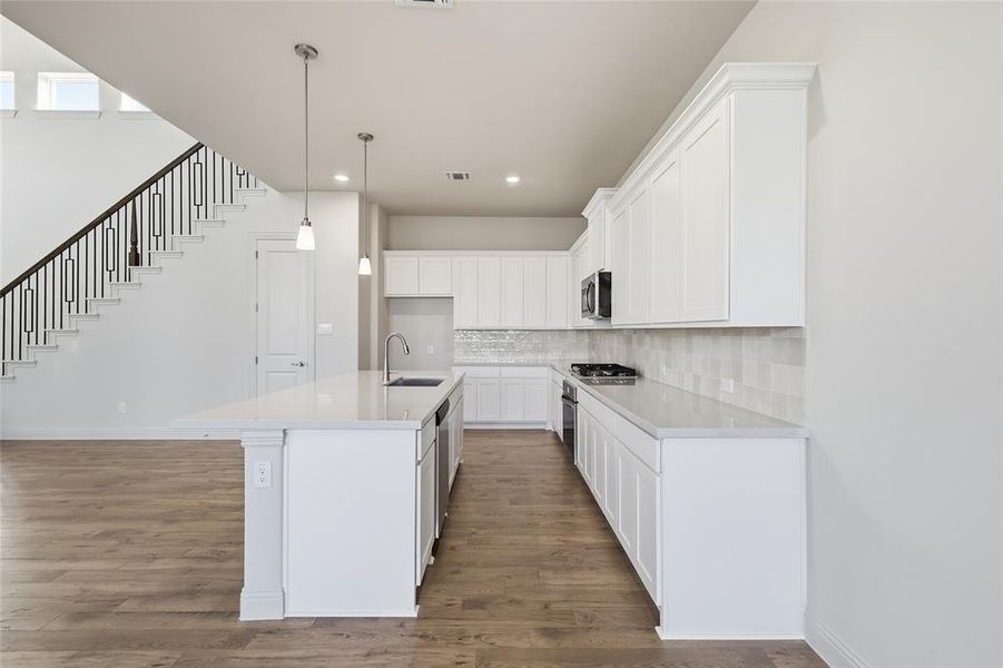 Kitchen with a kitchen island with sink, hanging light fixtures, white cabinetry, backsplash, and dark wood-style floors