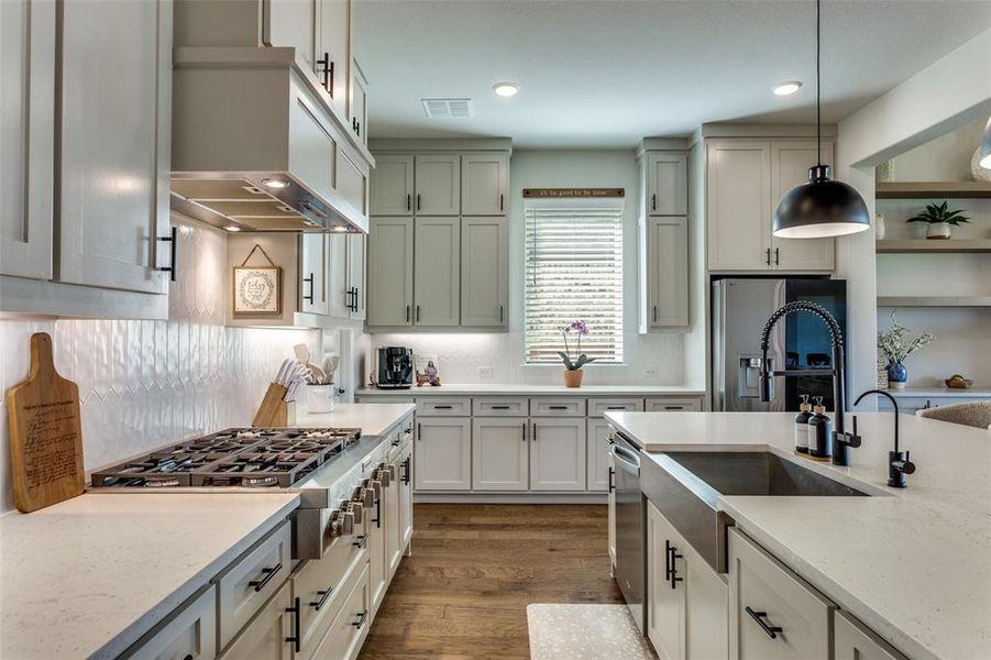 Kitchen with light stone countertops, decorative light fixtures, appliances with stainless steel finishes, dark wood-style flooring, and ventilation hood Kitchen with light stone countertops, decorative light fixtures, appliances with stainless steel finishes, dark wood-style flooring, and ventilation hood