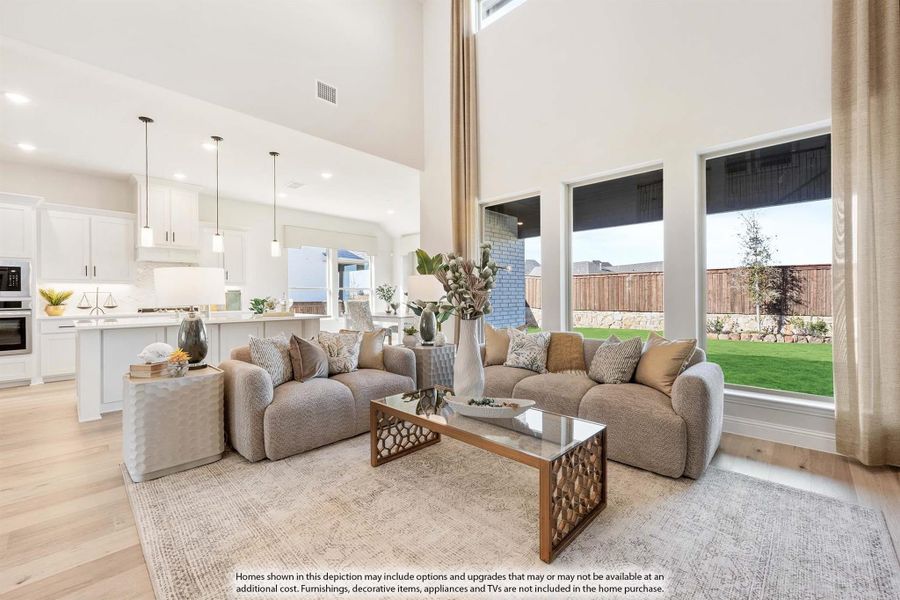 Open-concept living room with two-story ceiling, large windows, sectional sofa, and white kitchen visible in background