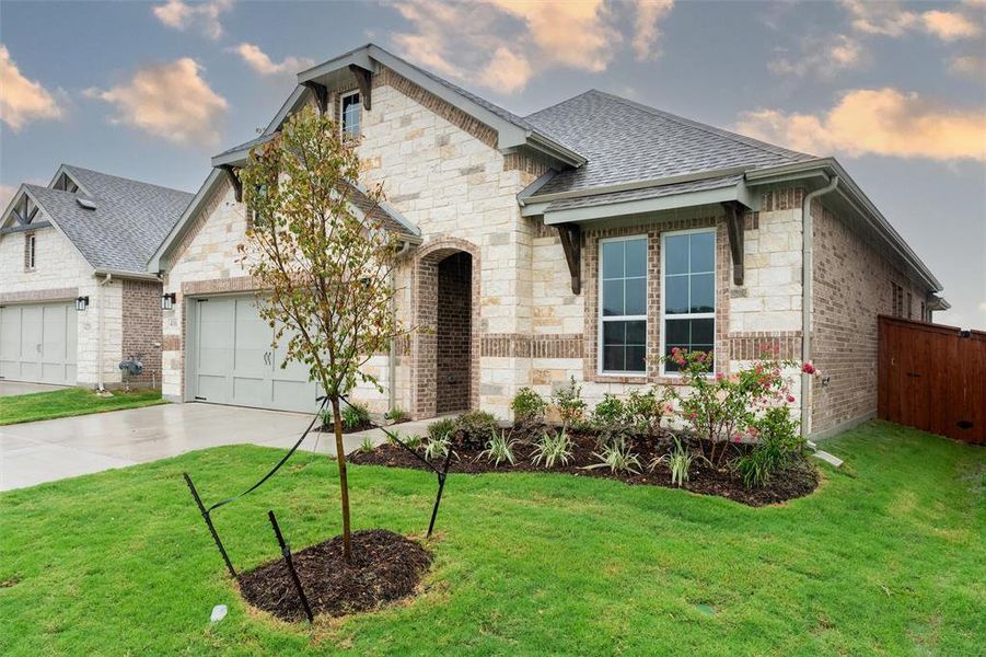 French country inspired facade featuring concrete driveway, an attached garage, stone siding, roof with shingles, and brick siding