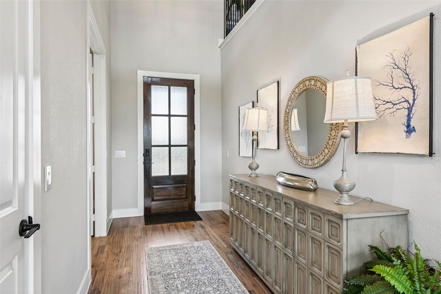 Entryway with dark wood glass-panel front door, hardwood floors, and decorative console table with mirror and lamps Entryway with dark wood glass-panel front door, hardwood floors, and decorative console table with mirror and lamps
