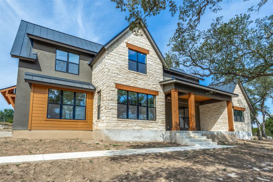 Back of property featuring a standing seam roof, stone siding, a porch, and stucco siding