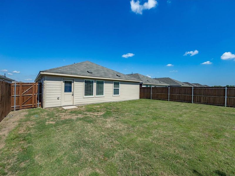 Expansive backyard featuring a manicured lawn, full perimeter privacy fencing, and direct exterior access