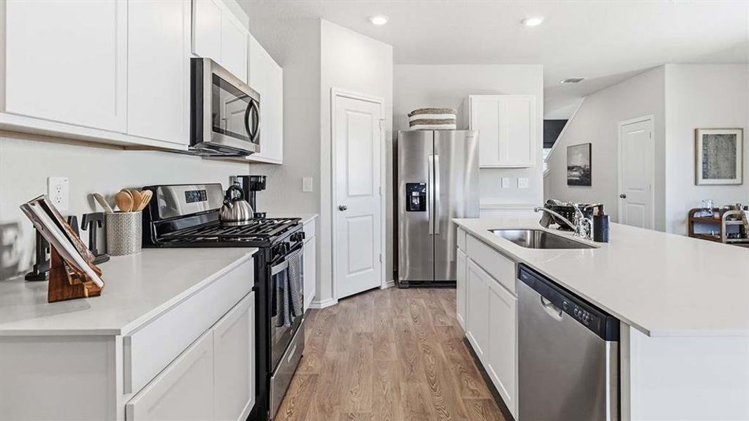 Modern kitchen featuring white cabinetry, light countertops, stainless steel appliances including a refrigerator, microwave, and dishwasher, and wood-finish flooring