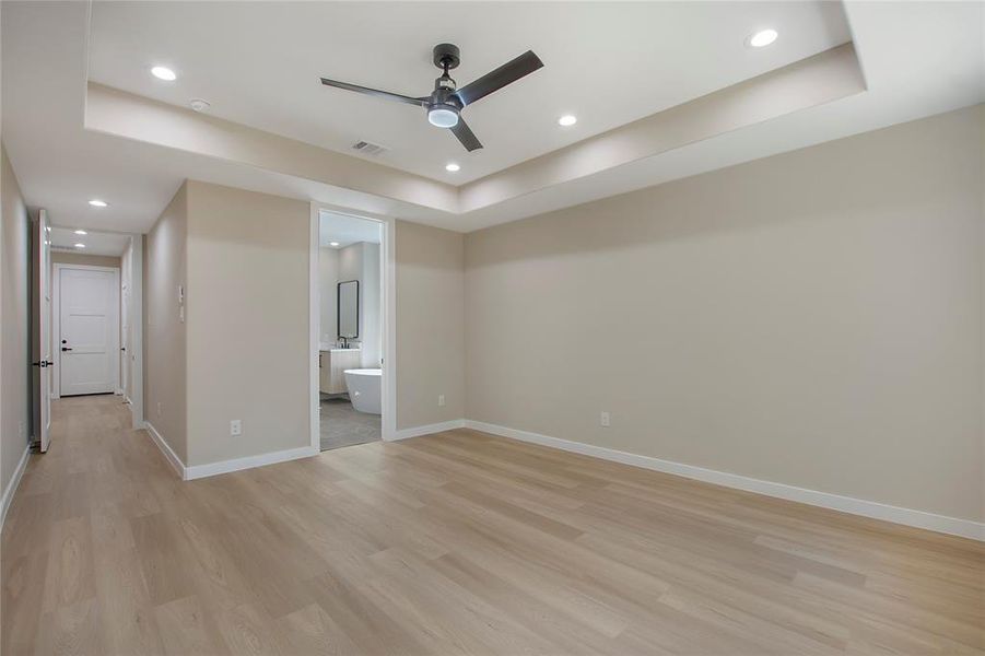 Unfurnished bedroom featuring light hardwood / wood-style floors, a raised ceiling, ensuite bathroom, and ceiling fan