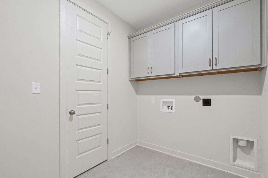 Laundry room featuring light gray cabinetry, wall-mounted utilities, and gray tile flooring Laundry room featuring light gray cabinetry, wall-mounted utilities, and gray tile flooring