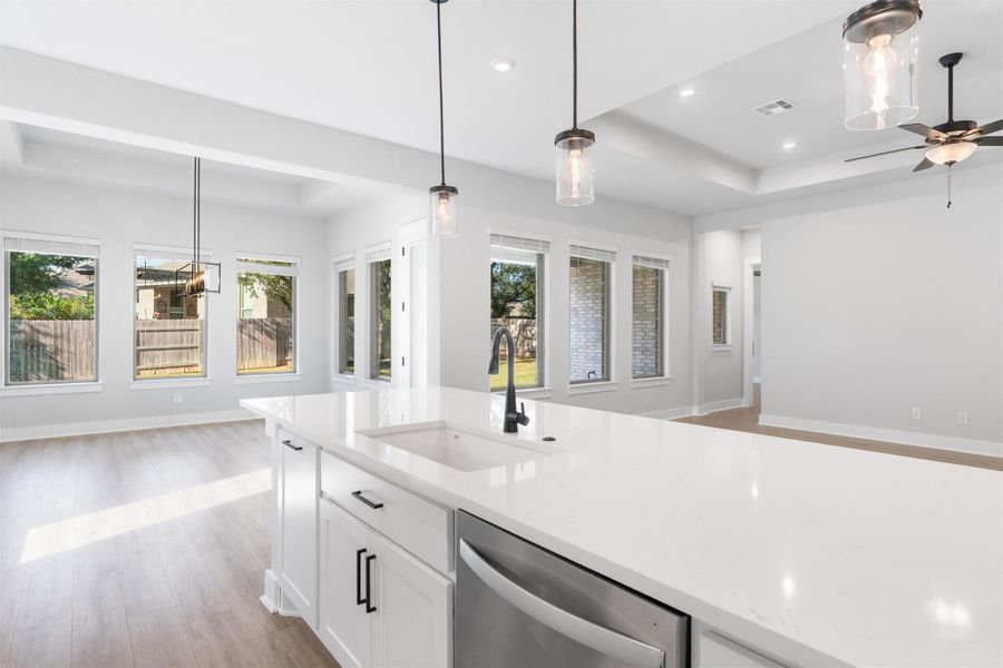 Kitchen with a tray ceiling, light wood-style floors, hanging light fixtures, white cabinetry, and recessed lighting