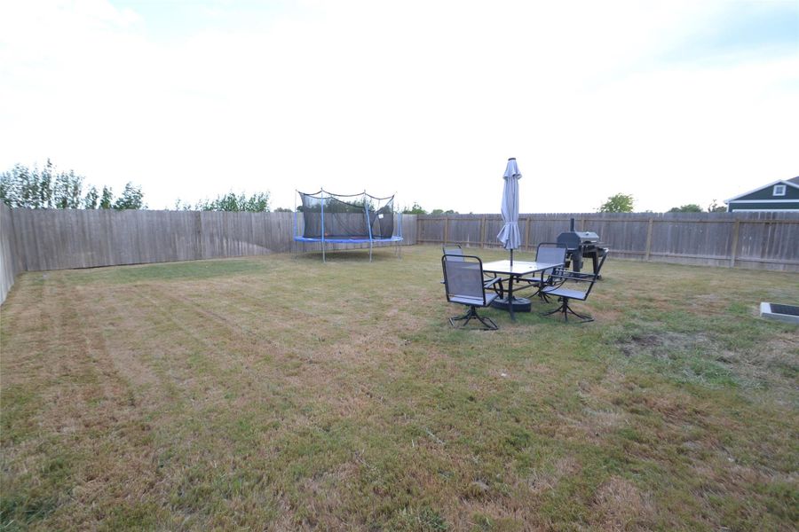 Fenced backyard featuring a trampoline