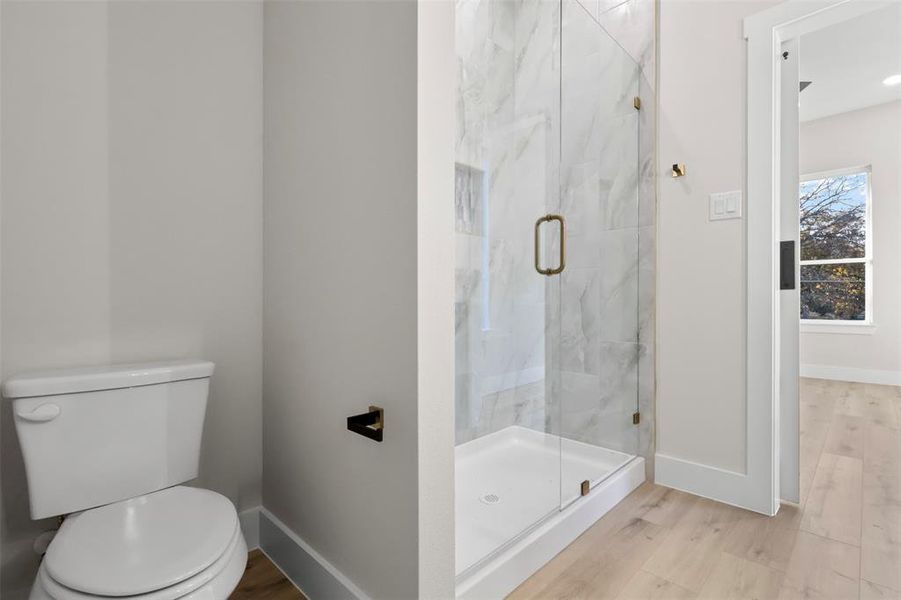 Bathroom with a shower with door, wood-type flooring, and toilet