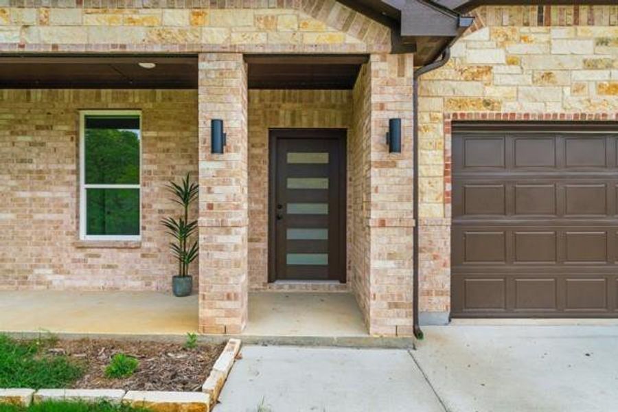 View of exterior entry featuring covered porch, a garage, and brick siding View of exterior entry featuring covered porch, a garage, and brick siding