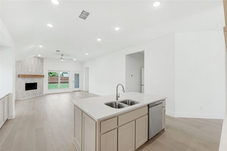 Kitchen island with double sink and dishwasher, open to living room with tile fireplace and light wood floors