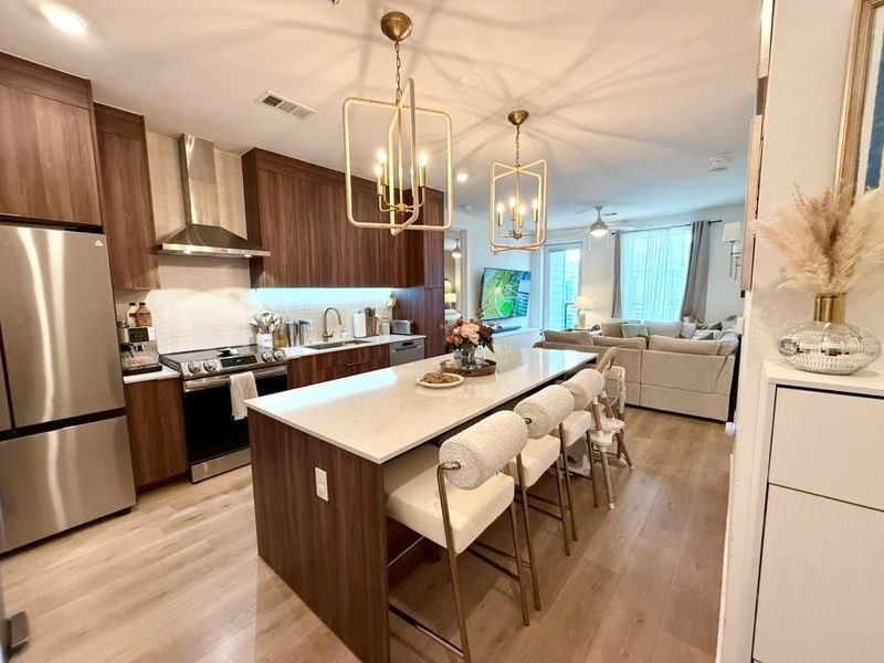 Kitchen featuring a kitchen breakfast bar, appliances with stainless steel finishes, wall chimney exhaust hood, a center island, and a chandelier