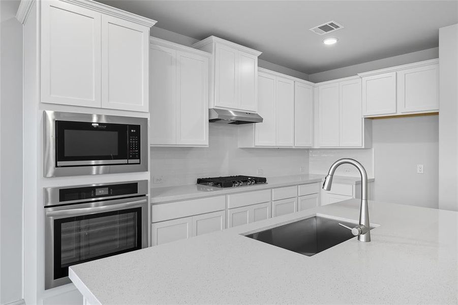 Kitchen with stainless steel appliances, light stone counters, white cabinets, under cabinet range hood, and recessed lighting Kitchen with stainless steel appliances, light stone counters, white cabinets, under cabinet range hood, and recessed lighting