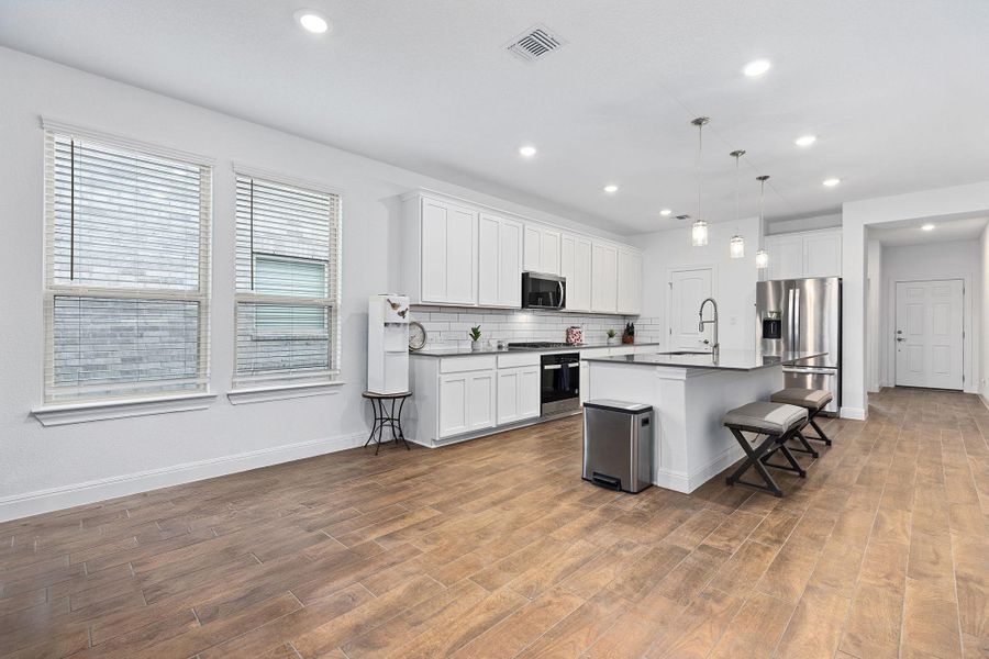 A well-lit, open-concept kitchen and living area showcases rich wood-look flooring and a modern aesthetic.