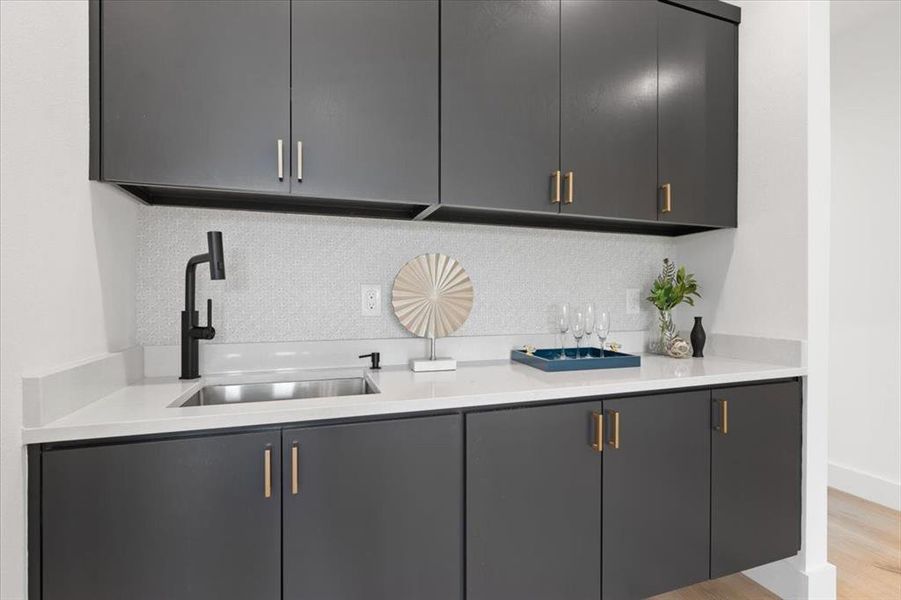 Bar featuring backsplash, sink, gray cabinetry, and light hardwood / wood-style flooring