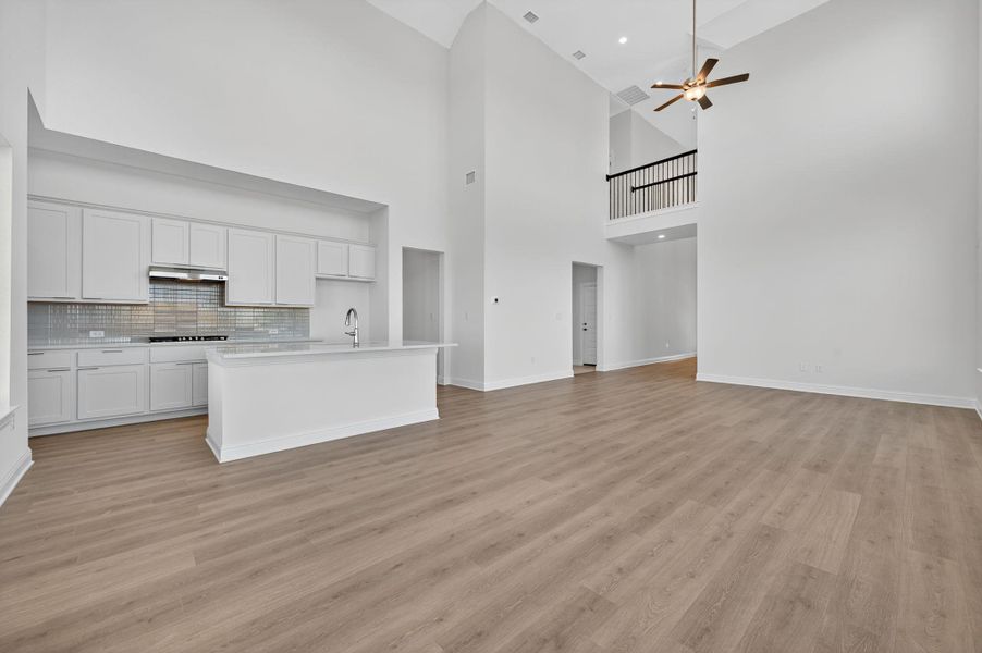 Unfurnished living room with light wood-style floors, ceiling fan, and a high ceiling