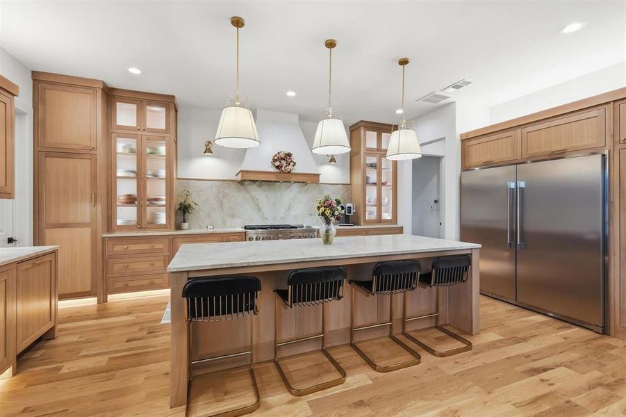 Kitchen featuring stainless steel built in refrigerator, a breakfast bar, a kitchen island, glass fronted cabinets, and light wood finished floors