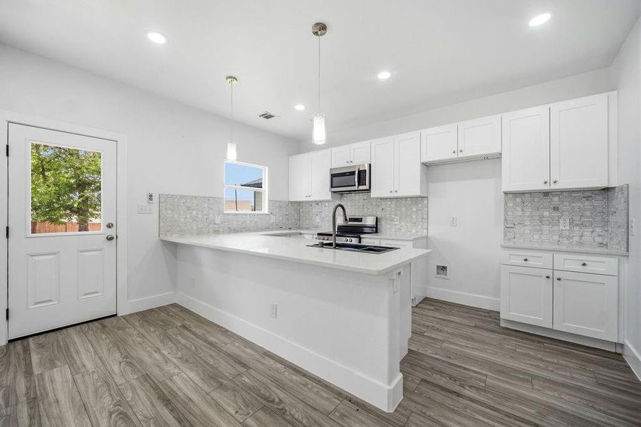 Modern kitchen featuring white shaker cabinetry, an integrated breakfast bar, a geometric tile backsplash, and wood-finish flooring Modern kitchen featuring white shaker cabinetry, an integrated breakfast bar, a geometric tile backsplash, and wood-finish flooring