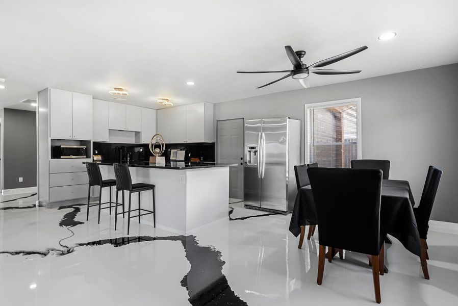 Kitchen with stainless steel appliances, an island with sink, a breakfast bar area, ceiling fan, and white cabinets