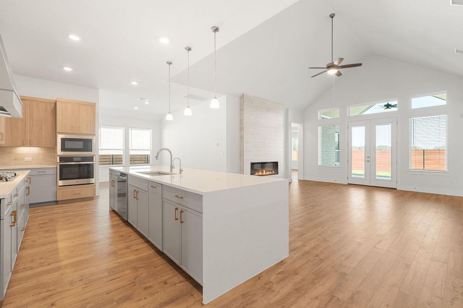 A well-lit kitchen with a spacious island gracefully transitions into a living area with a fireplace and vaulted ceilings.