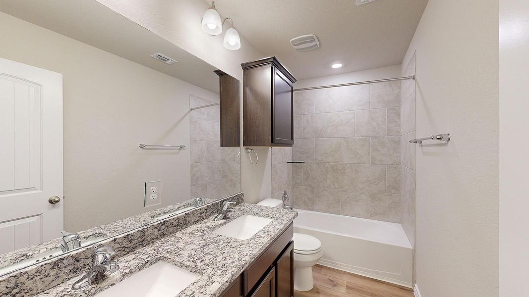 Bathroom featuring double vanity, bathtub / shower combination, and light wood-style floors