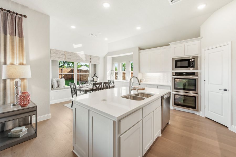 Open kitchen with white cabinets, center island with sink, stainless steel appliances, and light wood floors opening to dining area.