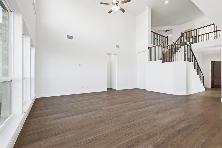 Unfurnished living room with dark wood-style floors, stairway, a towering ceiling, ceiling fan, and recessed lighting Unfurnished living room with dark wood-style floors, stairway, a towering ceiling, ceiling fan, and recessed lighting