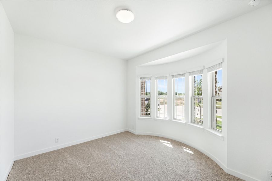 Empty bedroom with beige carpet, white walls, and a curved bay window with multiple panes