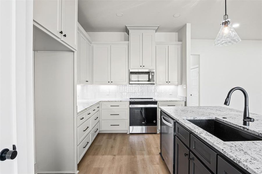 Kitchen featuring appliances with stainless steel finishes, hanging light fixtures, light stone countertops, light wood-style flooring, and white cabinetry Kitchen featuring appliances with stainless steel finishes, hanging light fixtures, light stone countertops, light wood-style flooring, and white cabinetry