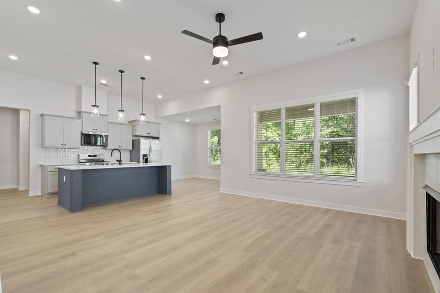 Open-concept living area featuring wood-finish flooring, a contemporary kitchen island with a light-colored countertop, and a fireplace with a white surround
