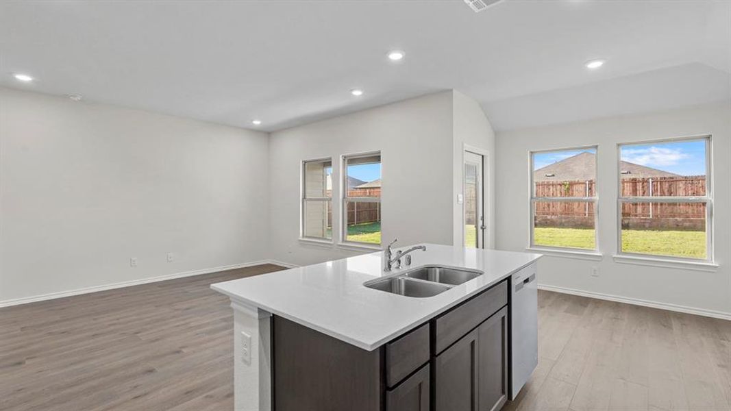 Kitchen with a kitchen island with sink, light wood-style floors, dark wood finish cabinets, light stone countertops, and dishwasher