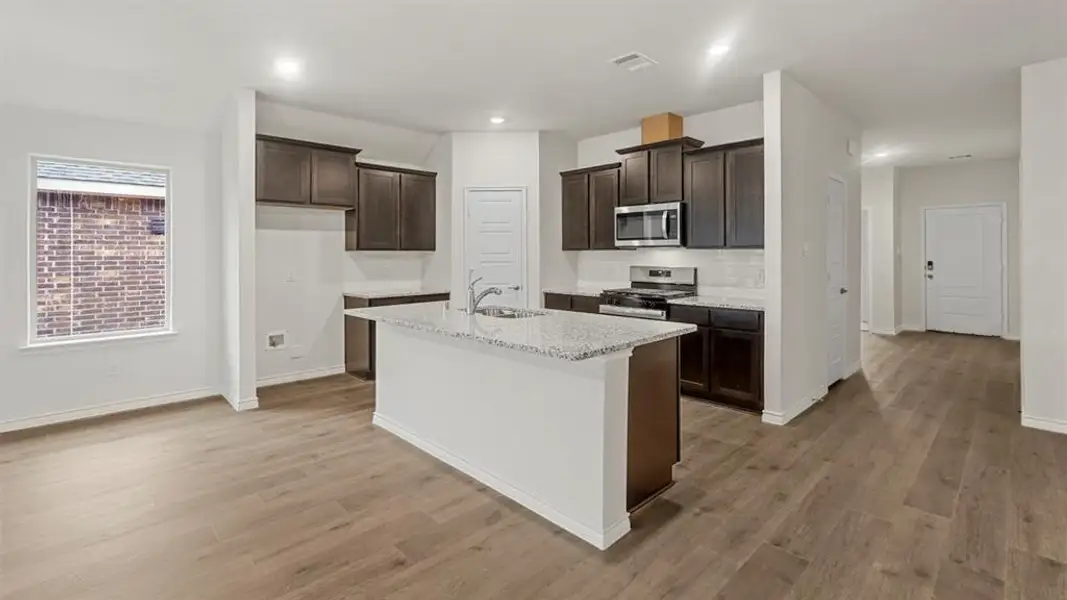 Open-concept kitchen featuring an island with a sink, dark wood-finish cabinetry, stainless steel appliances, speckled stone countertops, and wood-finish flooring