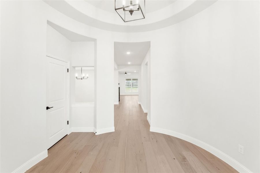 Entryway foyer with tray ceiling, metal chandelier, light hardwood floors, and hallway leading to main living area.
