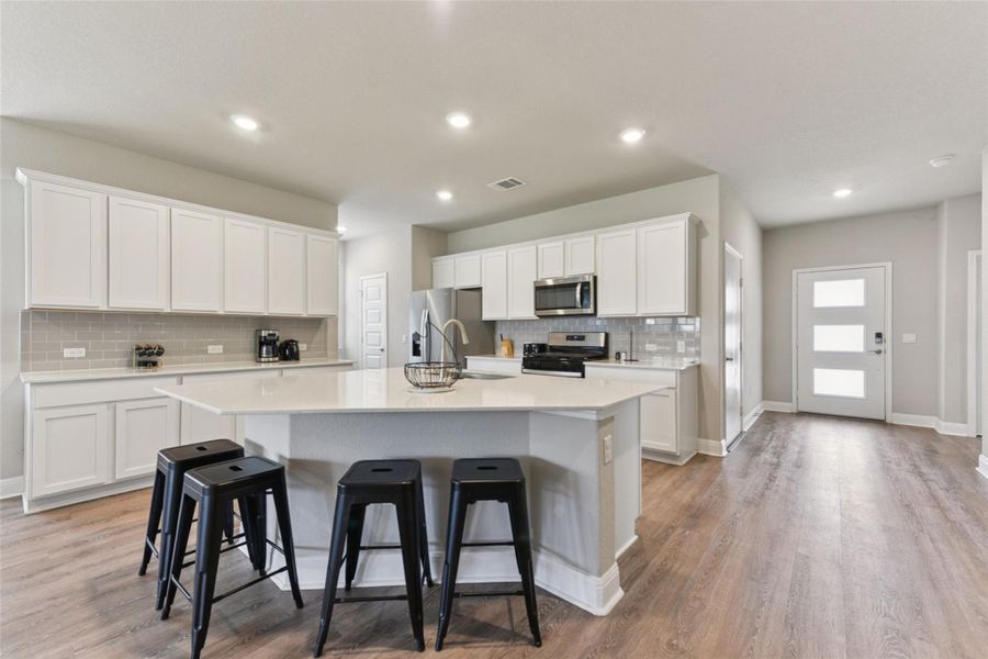 Kitchen featuring tasteful backsplash, a center island with sink, light countertops, a breakfast bar, and recessed lighting Kitchen featuring tasteful backsplash, a center island with sink, light countertops, a breakfast bar, and recessed lighting
