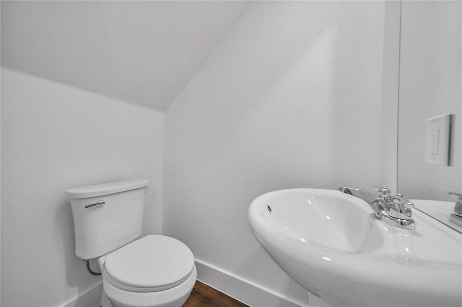 Half bathroom with a sink, toilet, wood finished floors, and baseboards